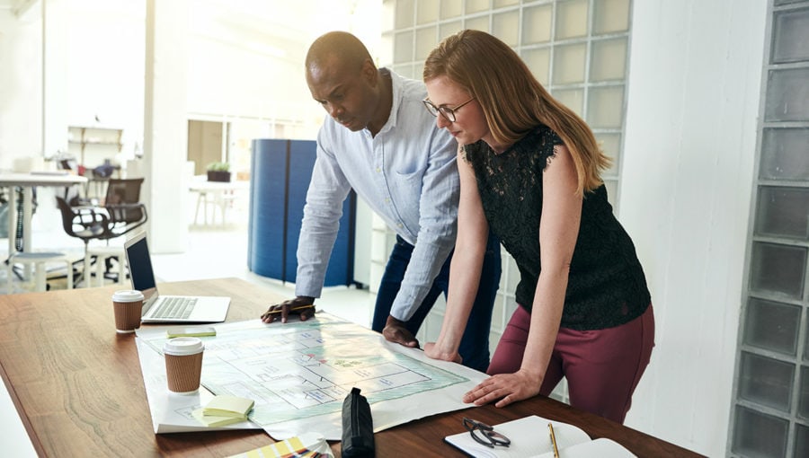 Man and woman looking over blueprints on desk.